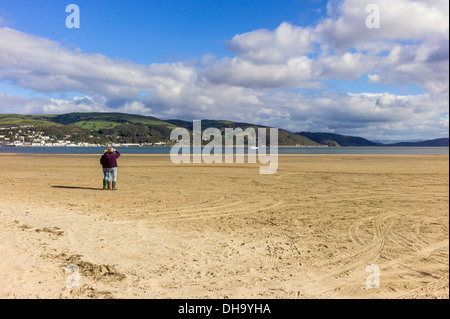 Adulto maschio e femmina stand in autunno la luce del sole su Ynyslas spiaggia sabbiosa la visione di una imbarcazione a vela motore fino al fiume Dovey Ceredigion Foto Stock