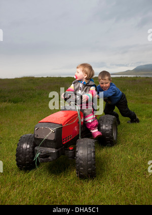 Ragazzo giovane spingendo la sua sorella più giovane sul trattore giocattolo, Eskifjordur, Islanda Foto Stock