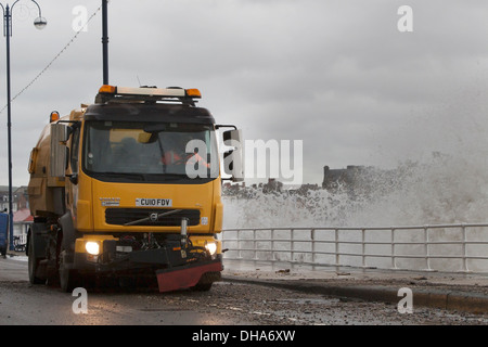 Roadsweeper inizia la pulizia dopo la tempesta in Aberystwyth con onde ancora le percosse la costa. Foto Stock