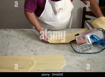 La donna casalinga che prepara la pasta, rolling out pasta attraverso la macchina Foto Stock
