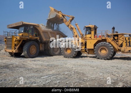 Azione girato di un caricatore a estremità anteriore il riempimento di una grande haul dump il mio carrello con terreno scavato. Settore minerario in Zambia, Africa. Foto Stock