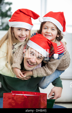 Giocoso Padre Piggybacking i bambini durante il periodo di Natale Foto Stock