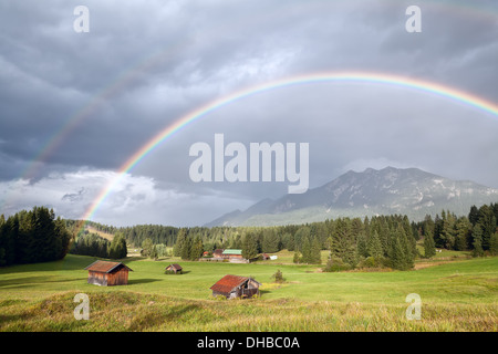 Arcobaleno colorato sopra prati alpini con capanne di legno, Baviera, Germania Foto Stock