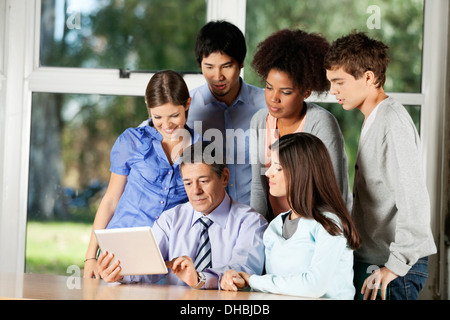 Insegnante con tavoletta digitale mentre gli studenti in piedi intorno a lui Foto Stock