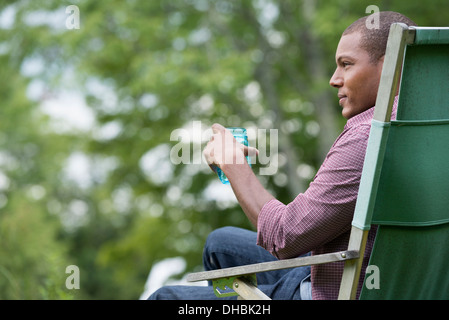Un uomo seduto in una sedia in un giardino rilassante. Foto Stock