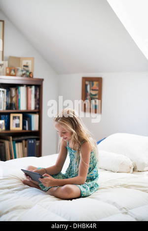 Una giovane ragazza seduta sul suo letto utilizzando una tavoletta digitale. Foto Stock