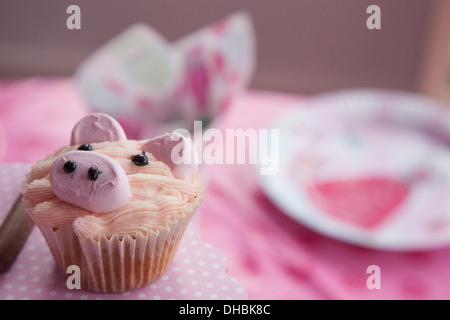 Una festa di compleanno, tavolo con un panno rosa e un cupcake decorato con l'immagine di un maiale. Foto Stock