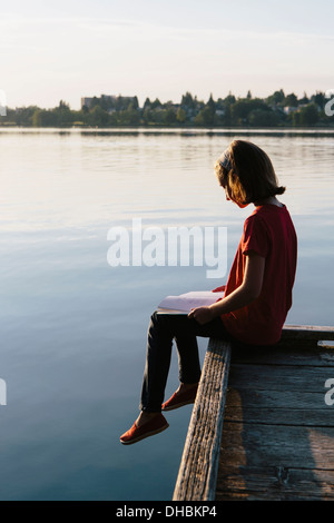 Una giovane ragazza seduta su un dock, la lettura di un libro. Foto Stock