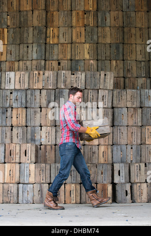 Un cortile. Una pila di tradizionali di cassette di legno per il confezionamento di frutta e verdura. Un uomo che porta una cassa vuota. Foto Stock