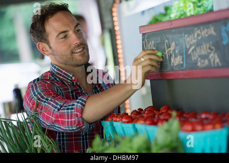 Un organico di frutta stand. Un uomo lo sfarinamento dei prezzi sulla lavagna. Foto Stock