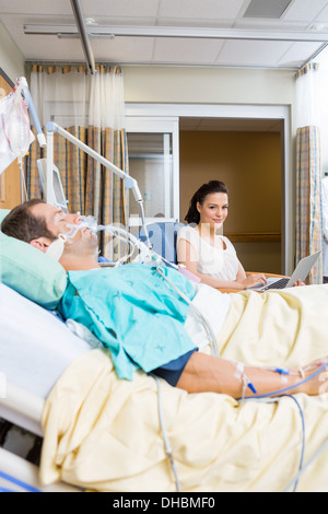 Donna con notebook seduta dal paziente in ospedale Foto Stock