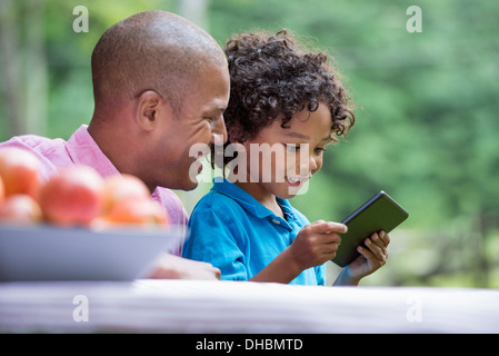 Un picnic sull'azienda. Fresca frutta organica sul tavolo. Un padre e figlio seduti insieme. Foto Stock