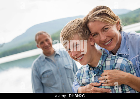 Una famiglia all'aperto sotto gli alberi su un lago. Due adulti e un ragazzino. Foto Stock