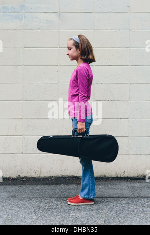 Una ragazza di 10 anni che trasportano un violino in un caso su una strada urbana. Foto Stock