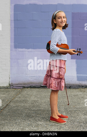 Una ragazza di 10 anni in possesso di un violino sotto il suo braccio e una prua nella sua mano. Foto Stock