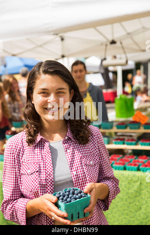 Una giovane ragazza in una fattoria stand tenendo una cestella di mirtilli. Foto Stock