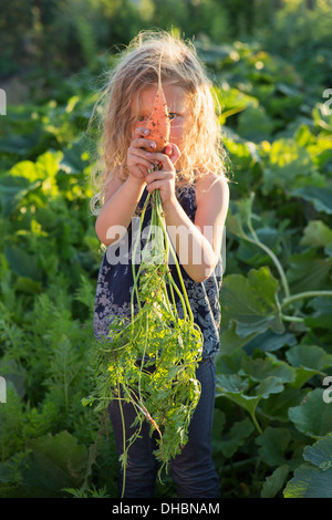 Una giovane ragazza con rosso lungo i capelli ricci all aperto in un giardino, tenendo appena raccolto le carote. Foto Stock