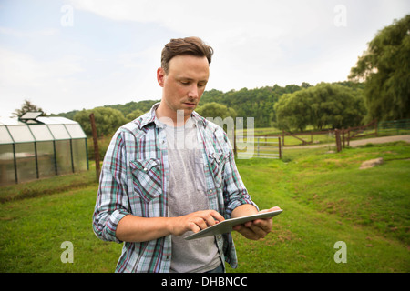 Un agriturismo biologico nelle Catskills Mountains. Un uomo con una tavoletta digitale in un paddock in erba. Foto Stock