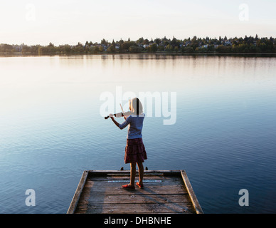 Una ragazza di 10 anni a suonare il violino all alba di un dock in legno. Foto Stock