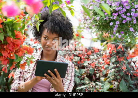 Una donna in un vivaio circondato da piante fiorite e foglie verdi. Foto Stock