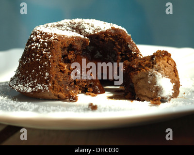 Primo piano di una torta lavica al cioccolato fuso isolata fatta in casa con un centro gooey e zucchero a velo sulla parte superiore, su un piatto bianco. Foto Stock