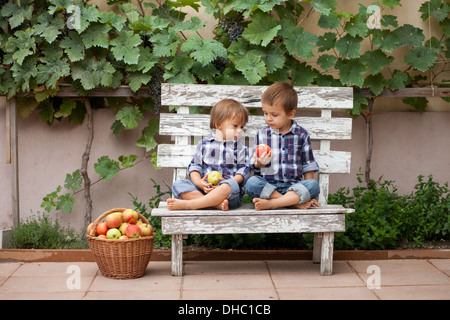 Due ragazzi con un cesto di mele, seduta su una panchina Foto Stock