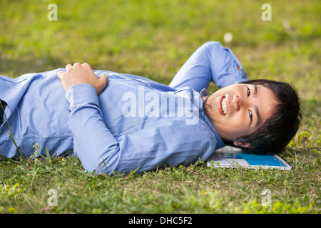 Studente maschio giacente su erba a college campus Foto Stock