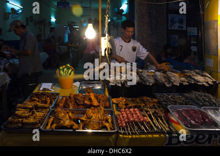 Ritratto orizzontale di un locale Lao uomo alla brace tutto il pesce alla griglia in corrispondenza di una strada cafe di notte. Foto Stock