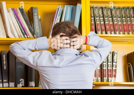 Lo studente tira i capelli contro scaffale in Biblioteca universitaria Foto Stock