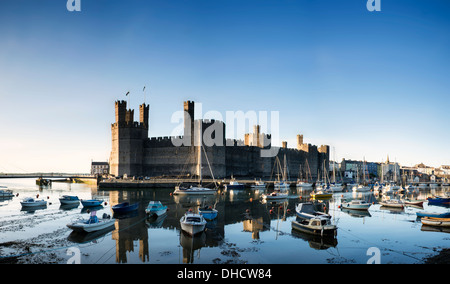 Bel tramonto su Caernarfon Castle in Galles con barche nel porto di bassa marea. Foto Stock