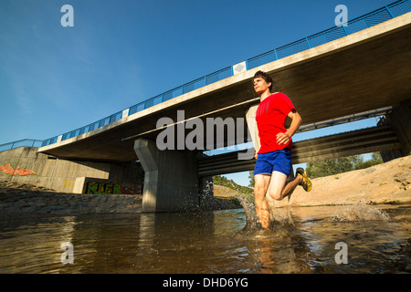 Germania Baden-Wuerttemberg, Winterbach, atletica giovane uomo che corre attraverso il fiume rem Foto Stock