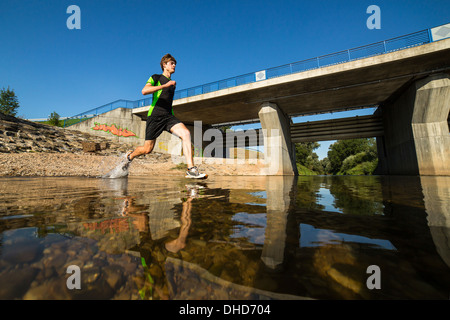 Germania Baden-Wuerttemberg, Winterbach, atletica giovane uomo che corre attraverso il fiume rem Foto Stock