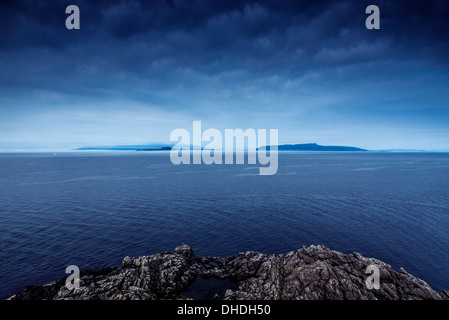 Moody Blue view delle piccole isole attraverso il mare da punto a Ardnamurchan, con uno sperone roccioso in primo piano. Foto Stock