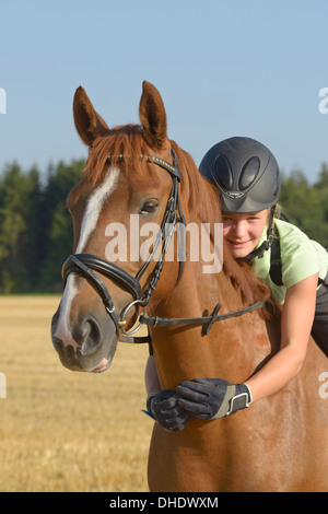 Tredici-anno-vecchia ragazza che indossa un casco e una protezione posteriore sul retro di un Irish Sport Pony cavallo Foto Stock