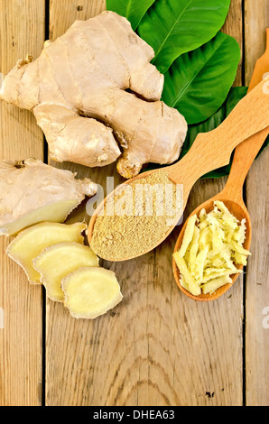 Grattugiato e lo zenzero in polvere in due cucchiai di legno, radice di zenzero, foglie verdi sullo sfondo del pannello di legno Foto Stock