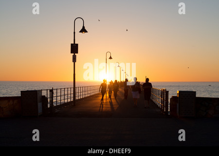 Persone che si godono una passeggiata al tramonto lungo il molo di Glenelg Jetty Australia in estate Foto Stock