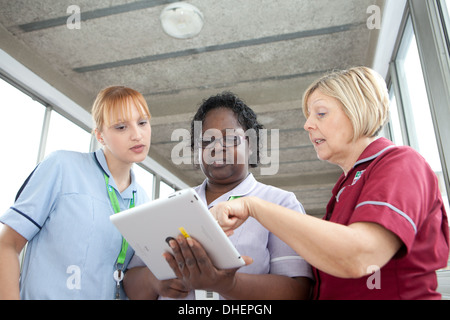 Tre infermieri utilizzare un iPad per guardare una pazienti note REGNO UNITO Foto Stock