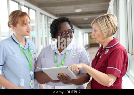 Tre infermieri utilizzare un iPad per guardare una pazienti note REGNO UNITO Foto Stock