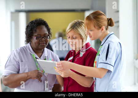 Un gruppo di tre infermieri discutere il lavoro su un computer tablet REGNO UNITO Foto Stock