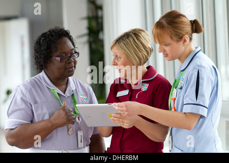 Un gruppo di tre infermieri discutere il lavoro su un computer tablet REGNO UNITO Foto Stock