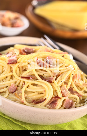 Spaghetti alla carbonara fatta con pancetta, uova, formaggio e pepe nero servito in tazza con formaggio alla griglia nel retro Foto Stock