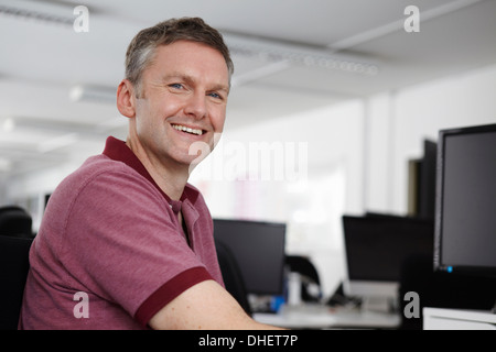 Uomo seduto alla scrivania con computer, sorridente in telecamera Foto Stock