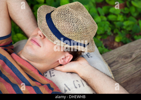 Giovane uomo che indossa cappello di paglia con le mani dietro la testa Foto Stock