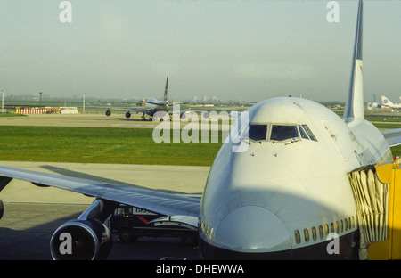 Due jumbo jet Boeing 747 all'aeroporto di Heathrow, uno di rullaggio e uno su un cancello Foto Stock