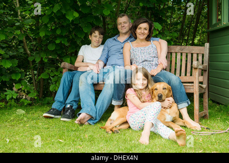 Ritratto di famiglia con due bambini seduti sulla panchina da giardino con il cane Foto Stock