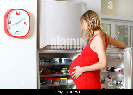 Donna incinta con craving cercando in frigo Foto Stock