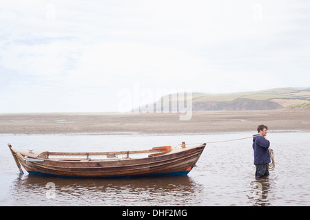 L'uomo tirando le barche a remi attraverso acqua, Wales, Regno Unito Foto Stock