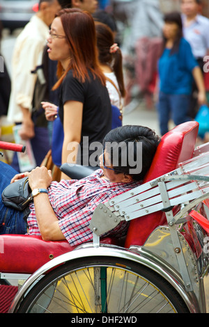 Dormire sul posto di lavoro. Ciclo turistica Rickshaw hawker dorme " al volante', Albert Street, Singapore. Foto Stock