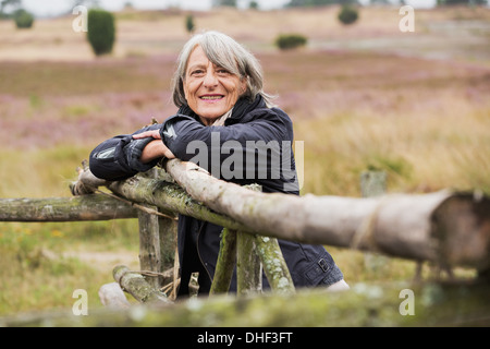 Senior donna appoggiata sulla staccionata in legno sorridente verso la telecamera Foto Stock