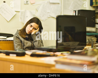 Annoiato giovane donna alla scrivania appoggiata sul raccordo a gomito Foto Stock